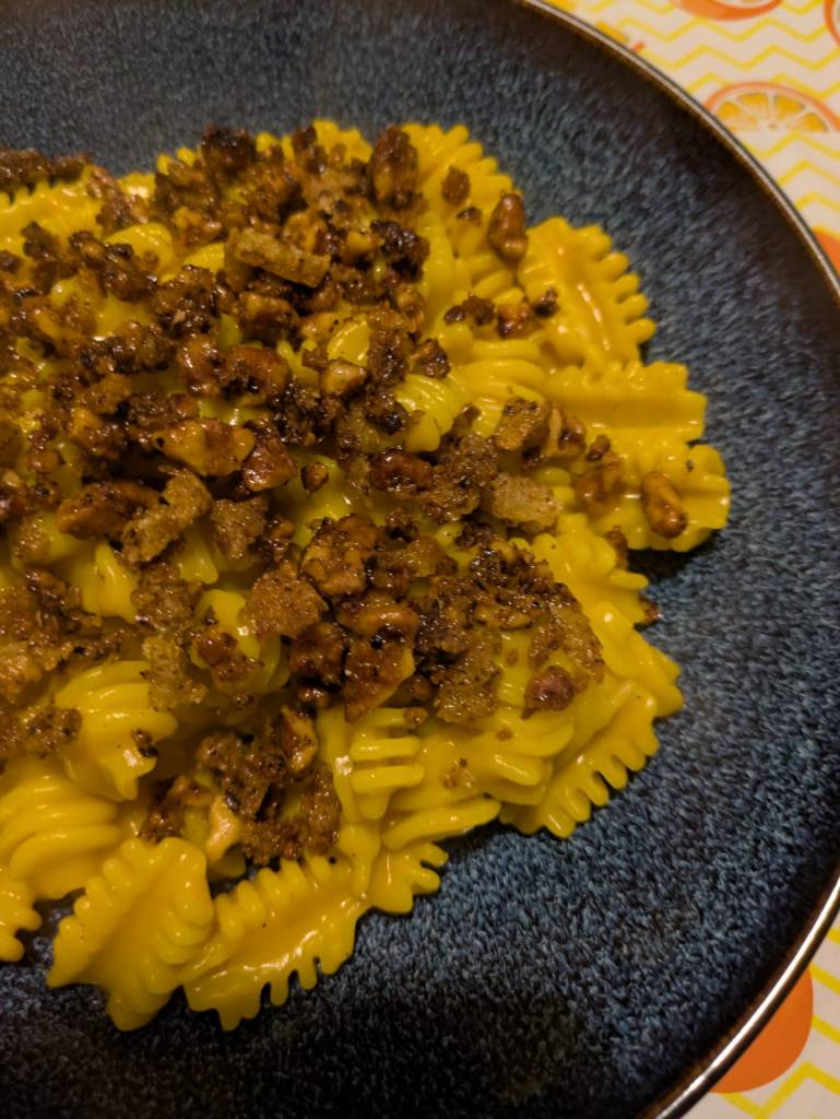 A blue bowl full of radiatori pasta with a bright yellow pumpkin and Gorgonzola sauce, topped with crispy walnut breadcrumbs.